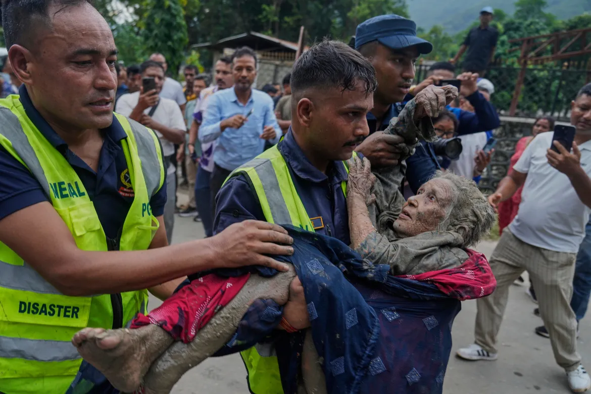 Nepal Police disaster response officers carrying an elderly woman covered in mud to safety
